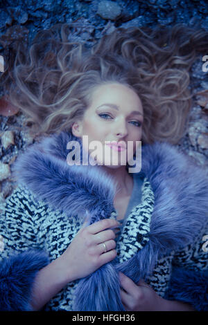 Photographic modeling as a career in the UK: A young slim attractive 20 year old caucasian woman girl with long blonde hair  lying on her back on the ground on a cold  frosty day looking like an Ice Queen Stock Photo