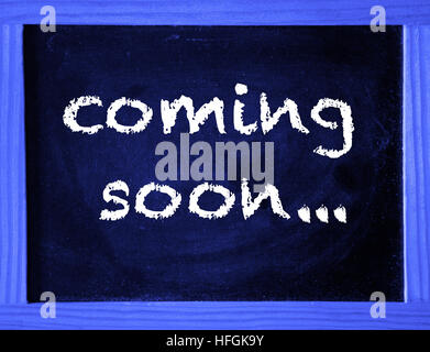 the words Coming Soon written on blue chalk board Stock Photo