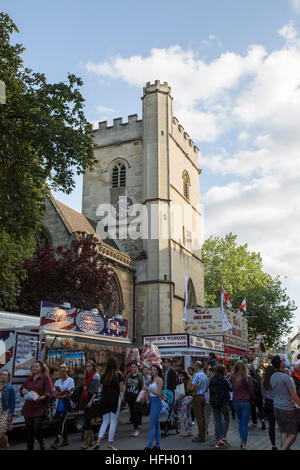 St Giles Fair in Oxford with people walking past stall selling a wide variety of food with the tower of St Michael's Church in the background Stock Photo