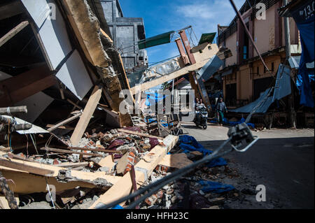 Beijing, Indonesia. 8th Dec, 2016. People pass a collapsed building at Meureudu market in Pidie Jaya district in Aceh, Indonesia, Dec. 8, 2016. A powerful earthquake hit the western Indonesian province of Aceh on Dec. 7, killing at least 97 people. © Veri Sanovri/Xinhua/Alamy Live News Stock Photo