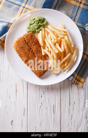 English food: fried fish in batter with chips and pea puree on a plate. vertical top view Stock Photo