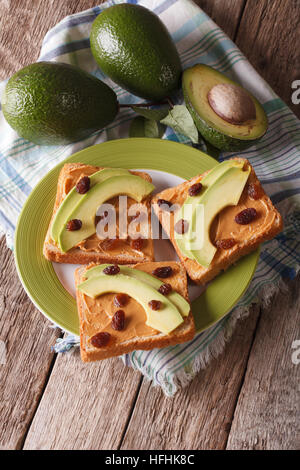 Homemade sandwiches with peanut butter, raisins and avocado close-up on a plate. vertical Stock Photo