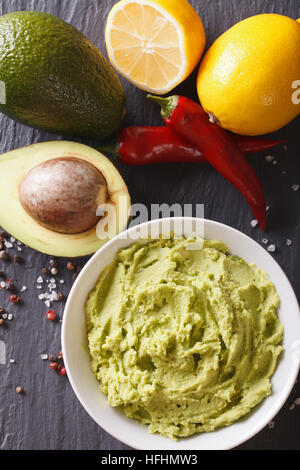 Mexican guacamole sauce with ingredients close-up on the table. vertical view from above