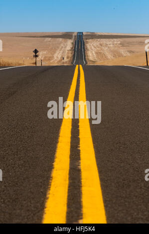 Bold yellow lines on a two lane blacktop highway running through golden wheat fields. Stock Photo