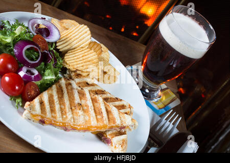 A typical English pub/bar snack of Cheese and Ham Toastie served with side salad, chips/ crisps and a glass of beer/ale. Stock Photo