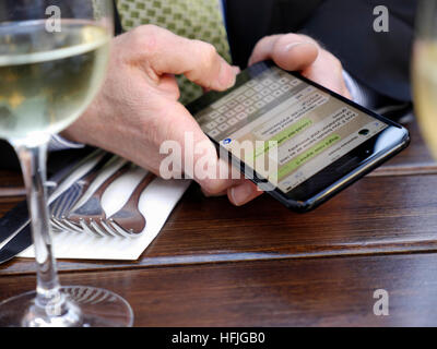 BUSINESS TEXTING CAFÉ Close-up on mature businessman's hands texting with his iPhone 7 plus smartphone sitting at alfresco Café restaurant situation with glass of white wine in foreground Stock Photo
