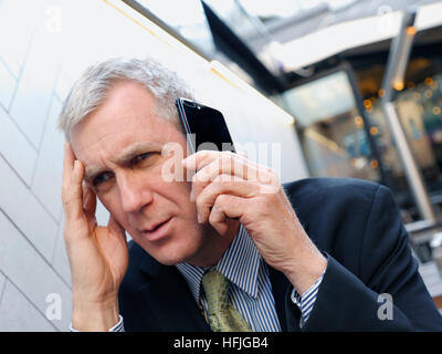 Worried businessman, bad news, looking concerned listening intently on his smartphone iPhone 7 plus mobile telephone at alfresco restaurant bar table Stock Photo