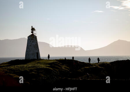 Visitors enjoying the view on  Llanddwyn Island with Twr Bach lighthouse silhouetted against the Llyn Peninsula mountain range Stock Photo
