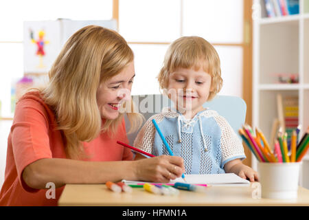 Happy family - mother and son toddler together paint. Adult woman helps to child boy. Stock Photo