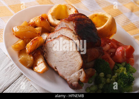 Sunday Roast: baked pork with potatoes, fresh vegetables and Yorkshire pudding on the plate closeup. horizontal Stock Photo