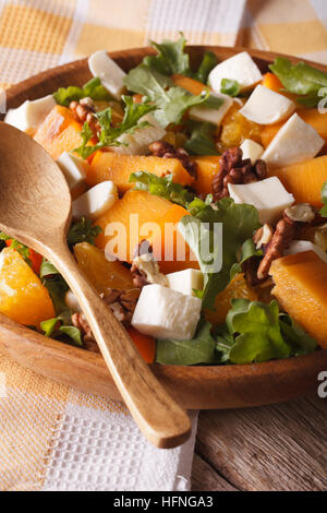 Fresh salad with persimmon, arugula and cheese close-up on the table. vertical Stock Photo