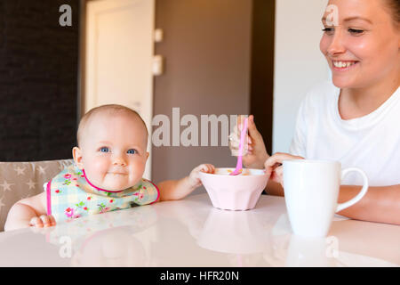 Caring young mother feeds her smiling baby girl Stock Photo
