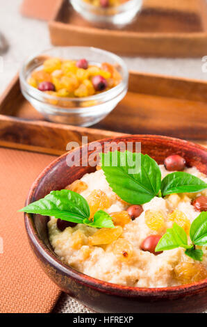 Close-up view of an old wooden bowl of healthy oatmeal with berries, raisins and herbs on a gray tablecloth with a blurred background