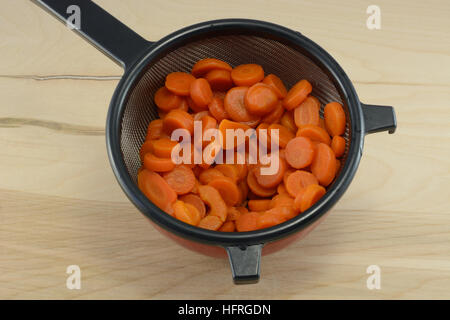 Rinsed sliced canned carrots draining in strainer in bowl to remove salt Stock Photo