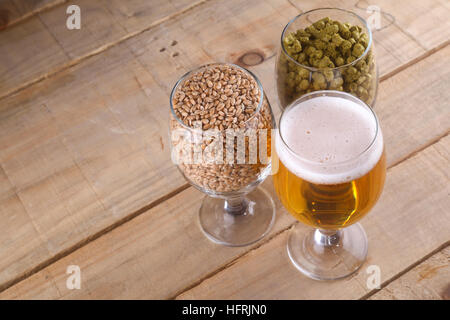 Glasses full of light beer, different types of malt and hops over a wooden background Stock Photo