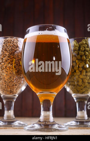 Glasses full of light beer, different types of malt and hops over a wooden background Stock Photo