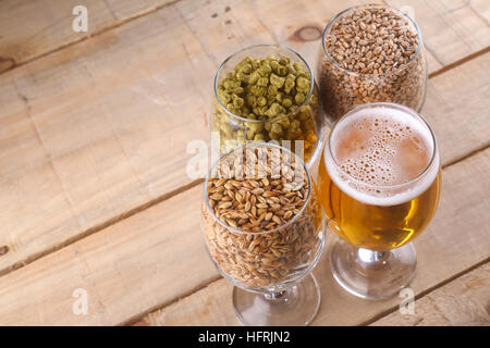 Glasses full of light beer, different types of malt and hops over a wooden background Stock Photo