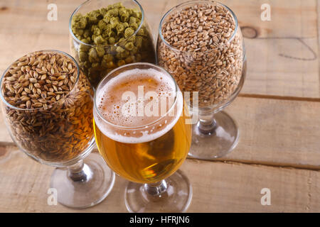 Glasses full of light beer, different types of malt and hops over a wooden background Stock Photo