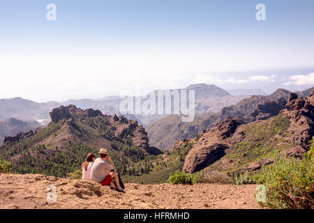 A young couple/hikers admire breathtaking views from Roque Nublo Mountain, one of the volcanic rocks on the island of Gran Canaria, Canary Islands, Sp Stock Photo