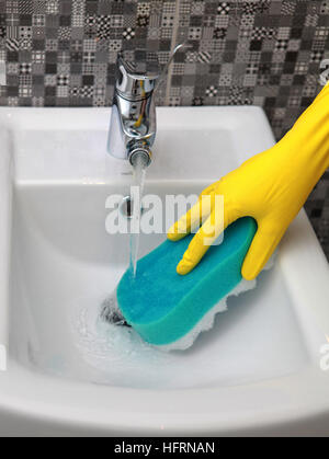 Hand in yelow glove with sponge washes sink Stock Photo