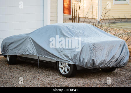 Sports car under silver colored cover outside a closed garage. Stock Photo