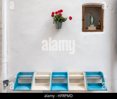 Shrine or street altar with a small statue of the virgin Mary, flowers and a blue and white bench in the white city Ostuni in Puglia, Italy. Stock Photo