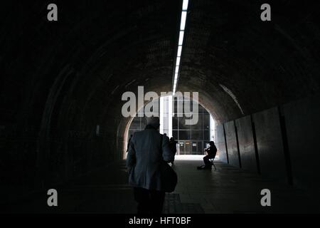 Musician and man walking in dark tunnel