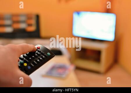 Holding the TV remote control and switching the channel on television. Stock Photo