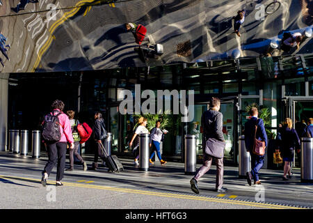 Passengers enter and exit the entrance to Birmingham New Street Railway Station. The modern materials reflect the people from above Stock Photo