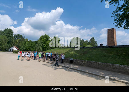 A large school party about to visit a  gas chamber and crematorium with a high raised chimney and covered in a grass mound where Jews and others victi Stock Photo