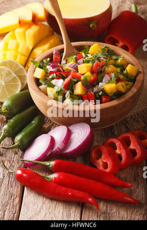 Salsa with mango, cilantro, onions and peppers close up in a bowl and ingredients on the table. vertical Stock Photo