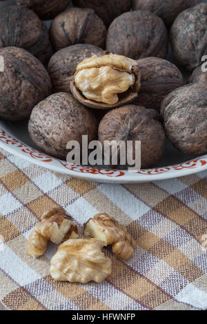 Whole walnuts and walnut kernels in white plate on table with checkered tablecloth Stock Photo