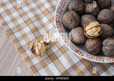 Whole walnuts and walnut kernels in white plate on table with checkered tablecloth Stock Photo