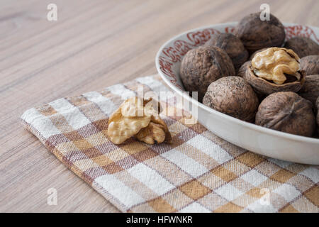 Whole walnuts and walnut kernels in white plate on table with checkered tablecloth Stock Photo