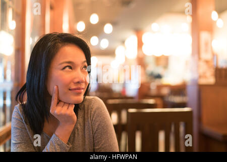 Tanned Asian girl thinking and looking upward to copy space, wondering menu to order for dinner, restaurant advertising concept Stock Photo