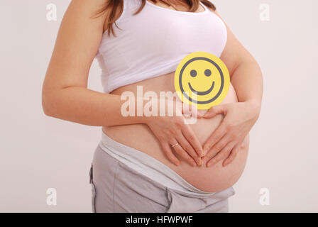 Pregnant woman clasped her hands in the shape of a heart on grey background Stock Photo