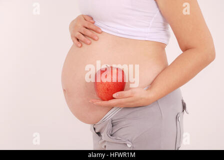 Pregnant woman holding apples in the hands of on grey background Stock Photo