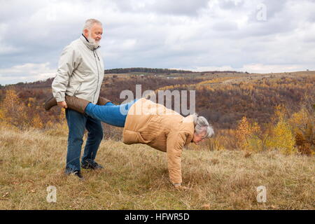 Elderly couple having fun and playing the wheelbarrow in nature. Stock Photo