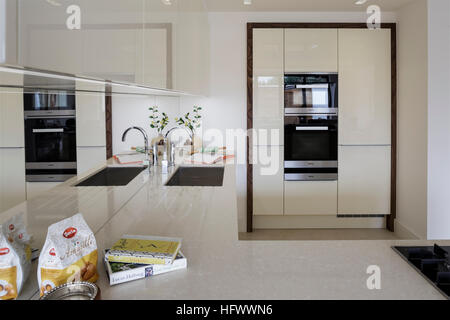 Sleek modern kitchen with white reflective cupboards and work surfaces Stock Photo