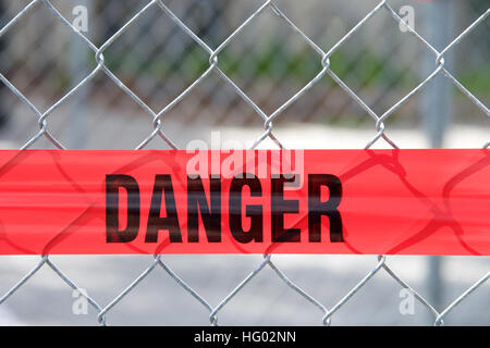 Red reflective danger barrier tape across a chain link fence to keep pedestrians out of construction zone, close up on word danger Stock Photo