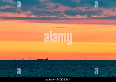 England, Whitstable. Distant Greater Gabbard wind farm, the London array, on horizon with deep orange dawn sky and dark clouds. Stock Photo