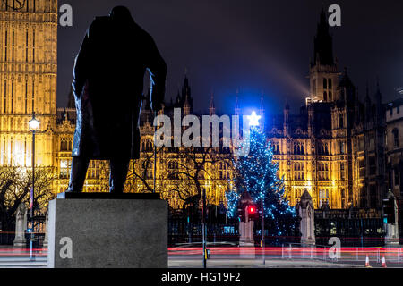 The Houses of Parliament's Christmas tree as seen from behind the Winston Churchill Statue of Parliament Square and the lights from cars and buses streak past the Queen Elizabeth II Tower which contains the bell known as Big Ben during long exposure photo Stock Photo