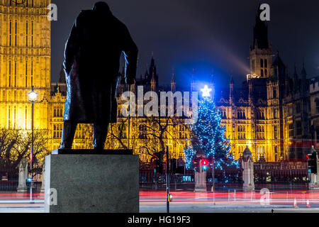 The Houses of Parliament's Christmas tree as seen from behind the Winston Churchill Statue of Parliament Square and the lights from cars and buses streak past the Queen Elizabeth II Tower which contains the bell known as Big Ben during long exposure photo Stock Photo