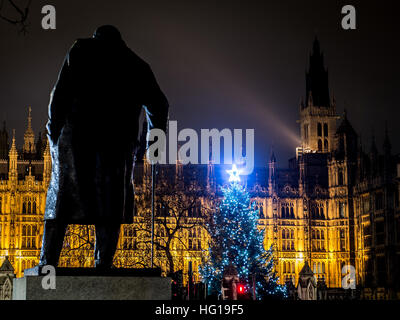 The Houses of Parliament's Christmas tree as seen from behind the Winston Churchill Statue of Parliament Square and the lights from cars and buses streak past the Queen Elizabeth II Tower which contains the bell known as Big Ben during long exposure photo Stock Photo