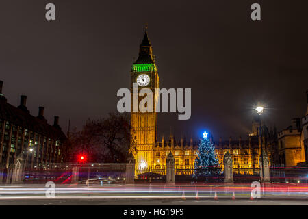 The Houses of Parliament's Christmas tree as seen from behind the Winston Churchill Statue of Parliament Square and the lights from cars and buses streak past the Queen Elizabeth II Tower which contains the bell known as Big Ben during long exposure photo Stock Photo