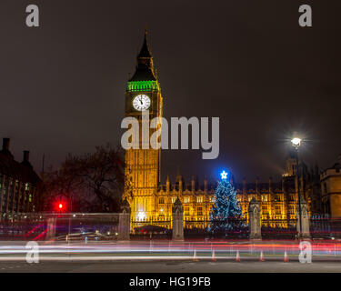 The Houses of Parliament's Christmas tree as seen from behind the Winston Churchill Statue of Parliament Square and the lights from cars and buses streak past the Queen Elizabeth II Tower which contains the bell known as Big Ben during long exposure photo Stock Photo