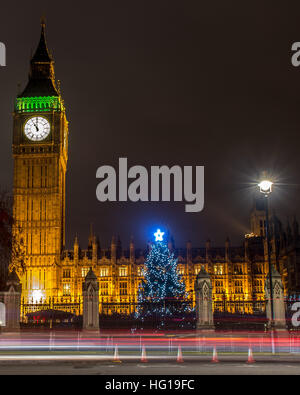 The Houses of Parliament's Christmas tree as seen from behind the Winston Churchill Statue of Parliament Square and the lights from cars and buses streak past the Queen Elizabeth II Tower which contains the bell known as Big Ben during long exposure photo Stock Photo