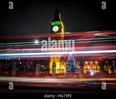 The Houses of Parliament's Christmas tree as seen from behind the Winston Churchill Statue of Parliament Square and the lights from cars and buses streak past the Queen Elizabeth II Tower which contains the bell known as Big Ben during long exposure photo Stock Photo