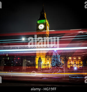 The Houses of Parliament's Christmas tree as seen from behind the Winston Churchill Statue of Parliament Square and the lights from cars and buses streak past the Queen Elizabeth II Tower which contains the bell known as Big Ben during long exposure photo Stock Photo