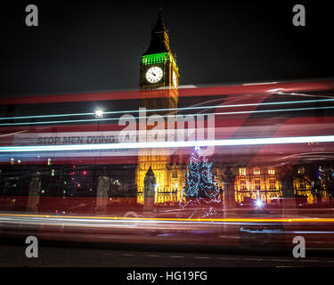 The Houses of Parliament's Christmas tree as seen from behind the Winston Churchill Statue of Parliament Square and the lights from cars and buses streak past the Queen Elizabeth II Tower which contains the bell known as Big Ben during long exposure photo Stock Photo